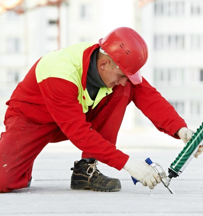 builder filling joint of concrete board with industrial polyurethane sealing foam in protective workwear at construction area